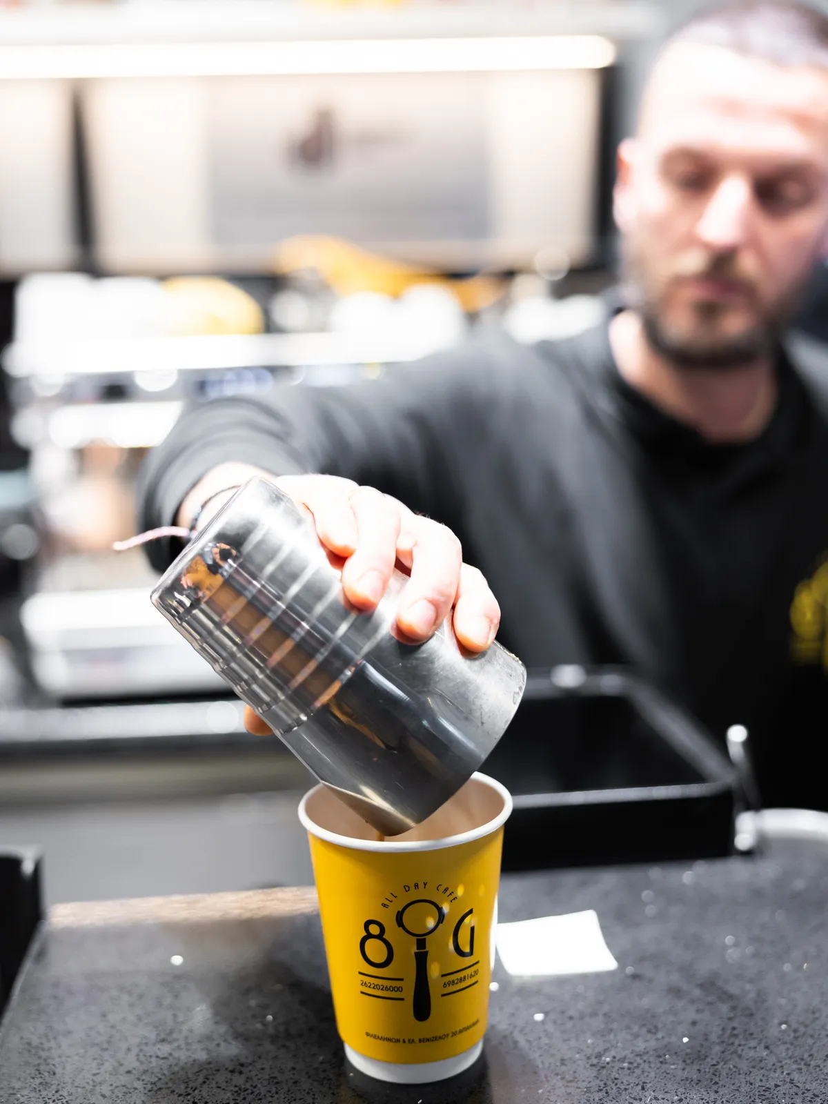 A barista at Eight Grams pours an iced coffee into the café’s yellow takeaway cup.